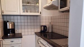 Eine kleine Küche mit weißen Schränken, einer Mikrowelle, einer Kaffeemaschine und einem Geschirrspüler.