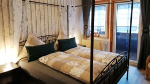 Un lit à baldaquin avec une literie à motifs, une tête de lit en bois et une vue sur un balcon avec une fenêtre et des rideaux.