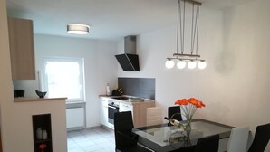 Une cuisine moderne avec des armoires blanches, une hotte noire et un four encastré. On y trouve une table à manger avec des chaises noires et un vase rempli de fleurs.