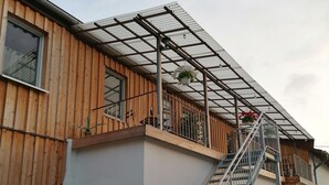 Un bâtiment à deux étages, avec une façade en bois, un escalier en métal et un balcon couvert.