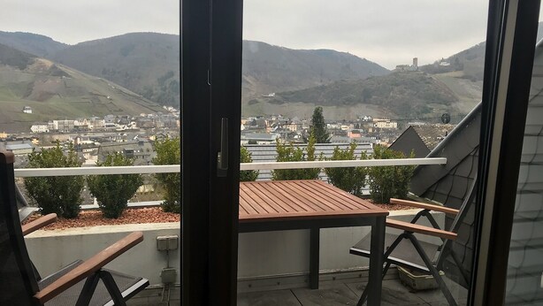 A balcony with a table and chairs, overlooking a town and mountains.