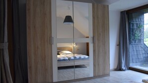 A bedroom with a bed, a wardrobe, and a window with a view of greenery.