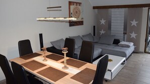 A modern living room with a dining table, chairs, a sofa, and a bed.