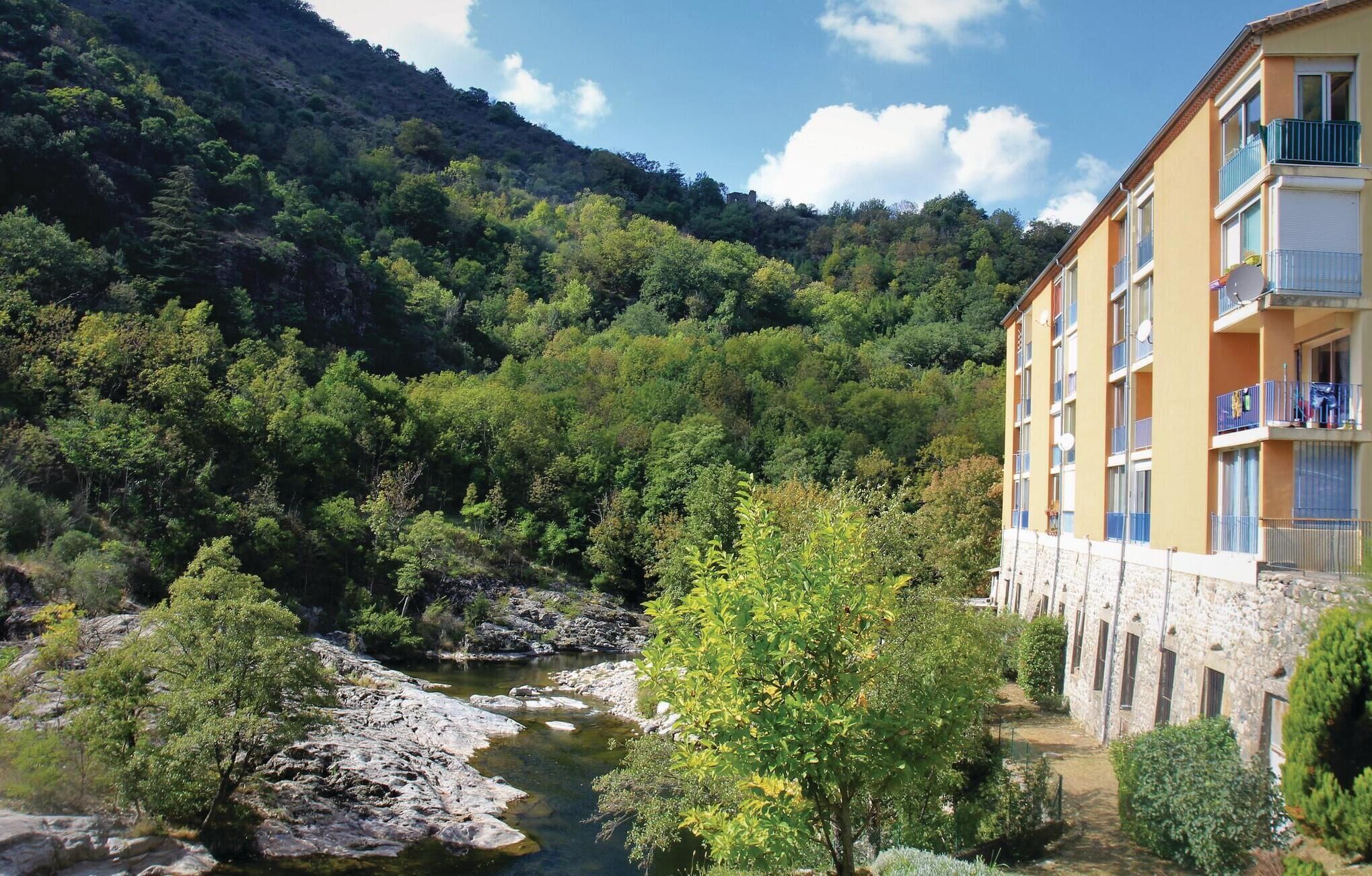 A hotel with a stone facade, multiple balconies, and a view of a river and forested hills.