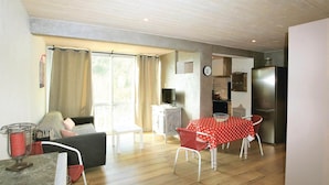 A living room with a sofa, a dining table with a polka dot tablecloth, a red chair, a small table with a basket, and a window with curtains. - Nice apartment in Vals les Bains (Vals les Bains)