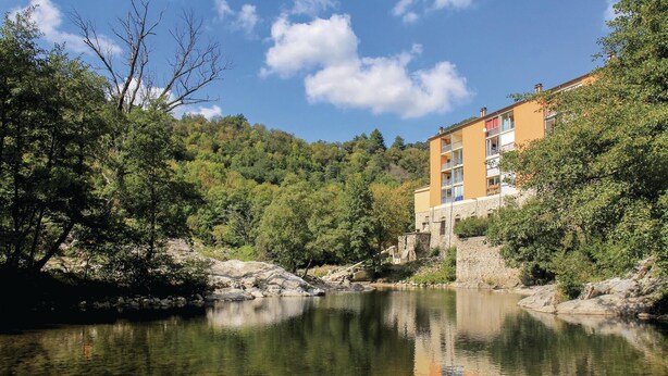 A hotel with a stone facade, multiple balconies, and a view of a river. - Nice apartment in Vals les Bains (Vals les Bains)