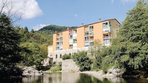 A multi-story hotel with balconies, located beside a river with a stone bridge leading to it. - Nice apartment in Vals les Bains (Vals les Bains)