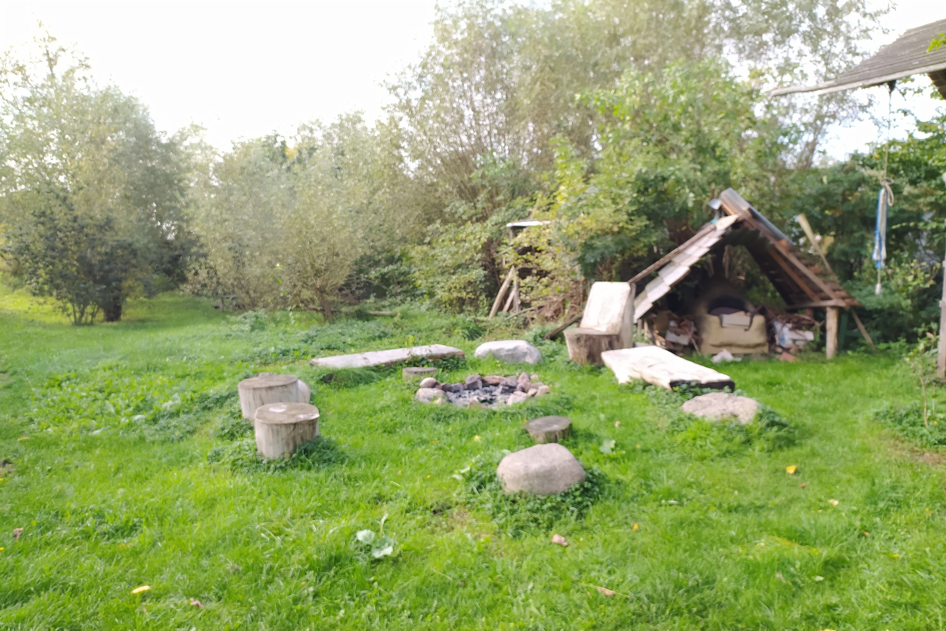 Un cadre extérieur rustique, avec une structure à toit de chaume, un foyer et des rochers disposés çà et là.