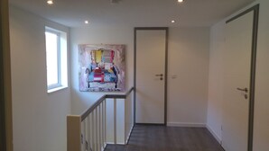 Un couloir avec une rambarde en bois, une porte et un tableau accroché au mur.