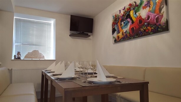 Un coin repas avec une longue table dressée pour le repas, un téléviseur fixé au mur et un tableau coloré au-dessus de la table.
