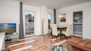 A modern living room with a TV, sofa, and dining area. - 3-room apartment Haus Godewind 10 in Binz, balcony, parking lot, beach chair on the beach (Binz)