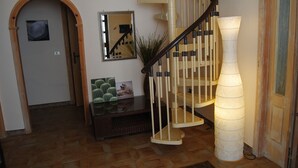 Escada com corrimão de madeira e degraus bege, espelho na parede e uma planta de cacto sobre uma mesa.