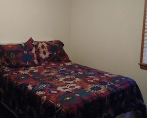 Una cama con una colcha estampada en una habitación con paredes lisas y una ventana con persianas.