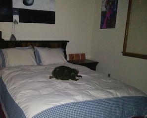 Una cama con un perro acostado encima, una mesita de noche y una pared con un cartel.