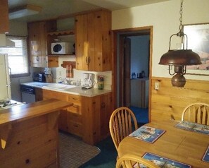 Cocina compacta con armarios de madera, microondas y comedor con mesa y sillas.