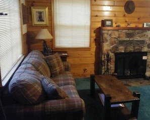 Una sala de estar acogedora con un sofá a cuadros, una mesa de centro de madera, una chimenea y una ventana con persianas.