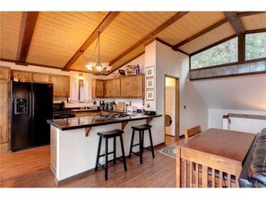 A kitchen with wooden beams, a black refrigerator, a wooden island with stools, and a dining table with chairs.