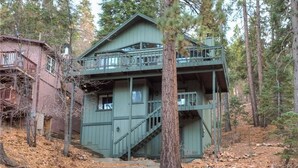 A two-story cabin with a balcony, surrounded by trees.