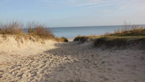 A sandy beach path leading to the sea, bordered by grassy dunes.