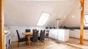 A modern kitchen with white cabinets, a wooden dining table, and a skylight.