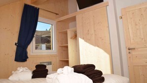 Une pièce en bois avec un lit, un téléviseur fixé au mur et une fenêtre avec un rideau.