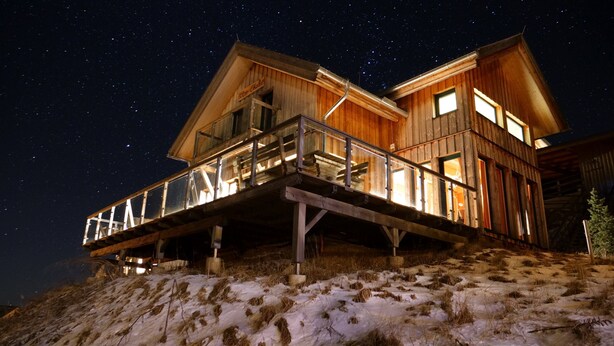 Une cabane en bois dotée d’un balcon, se dressant sous un ciel étoilé.