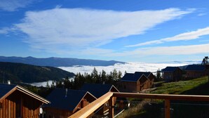 Un chalet de montagne avec des cabanes en bois, une terrasse en bois et une vue sur les montagnes et les nuages qui les surplombent.