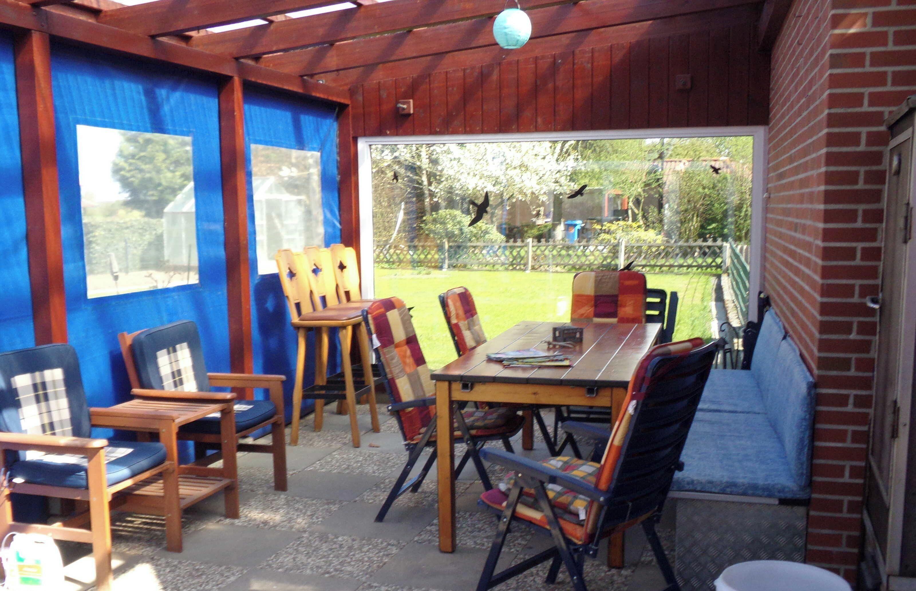Una veranda esterna con mobili in legno, un tavolo e vista sul giardino.