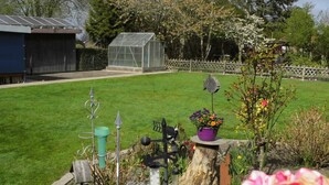 A well-maintained garden with a variety of plants and flowers, a small greenhouse, and a wooden fence. - At the ice cream parlor, Germany (Pahlen)