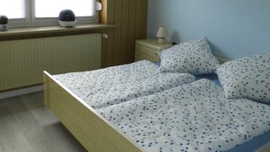 A bedroom with a bed, a window, a radiator, and a bedside table with a lamp. - At the ice cream parlor, Germany (Pahlen)