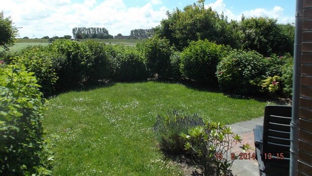 Ein Garten mit Rasen, Büschen und einer Ziegelmauer.