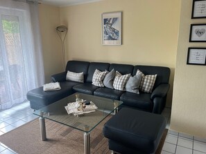 Een woonkamer met een zwarte leren bank, een glazen salontafel en een geruit tapijt.
