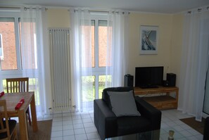 A living room with a black sofa, a wooden coffee table, a TV on a wooden stand, and a dining table with chairs.