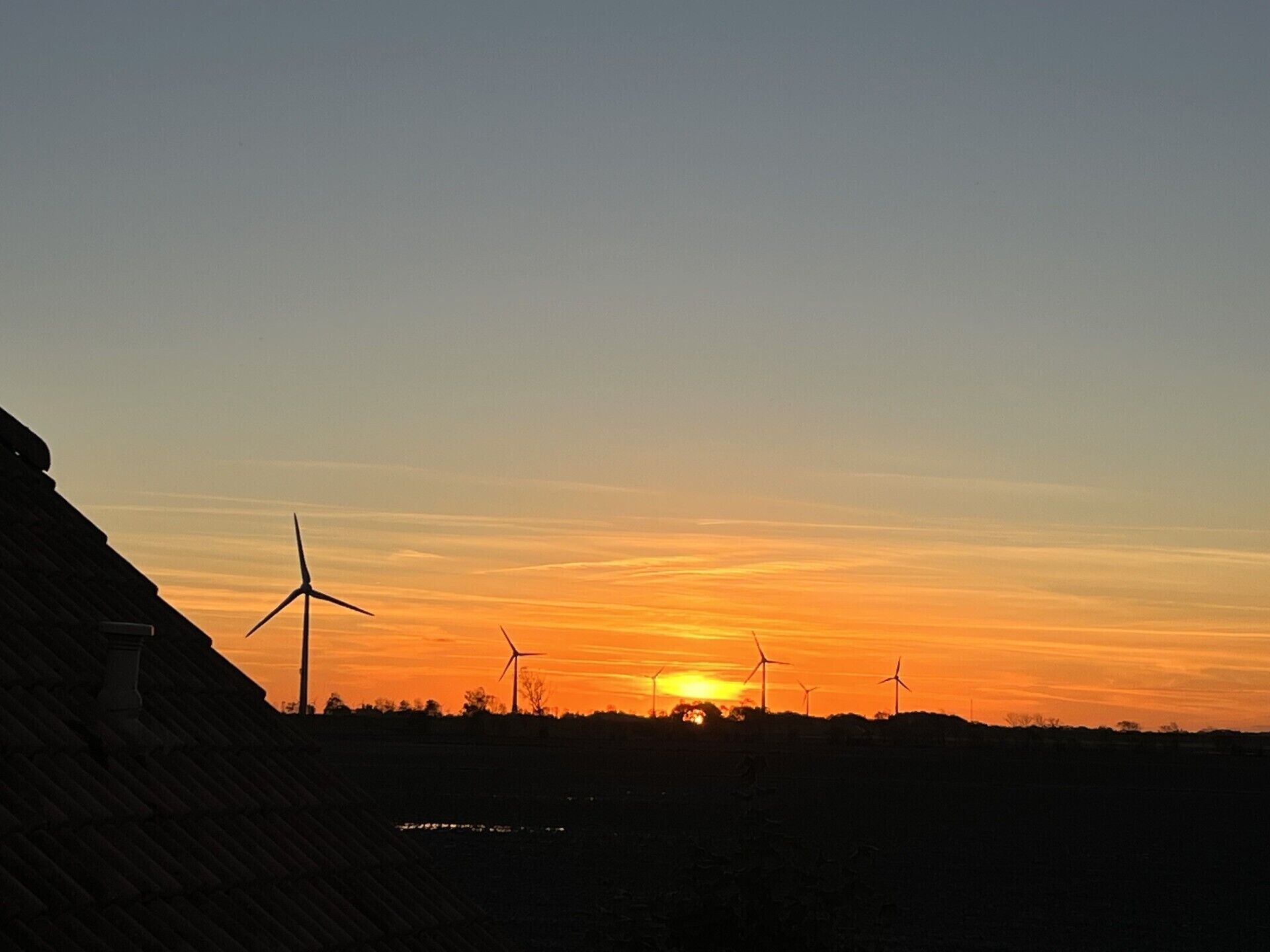 Un atardecer con siluetas de aerogeneradores contra el cielo.