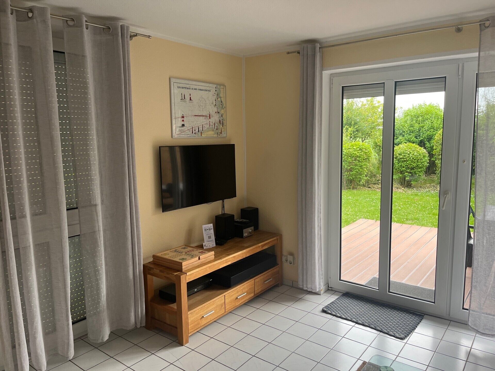 Une pièce avec un téléviseur posé sur un meuble en bois, une carte accrochée au mur et une porte-fenêtre coulissante donnant sur un jardin.