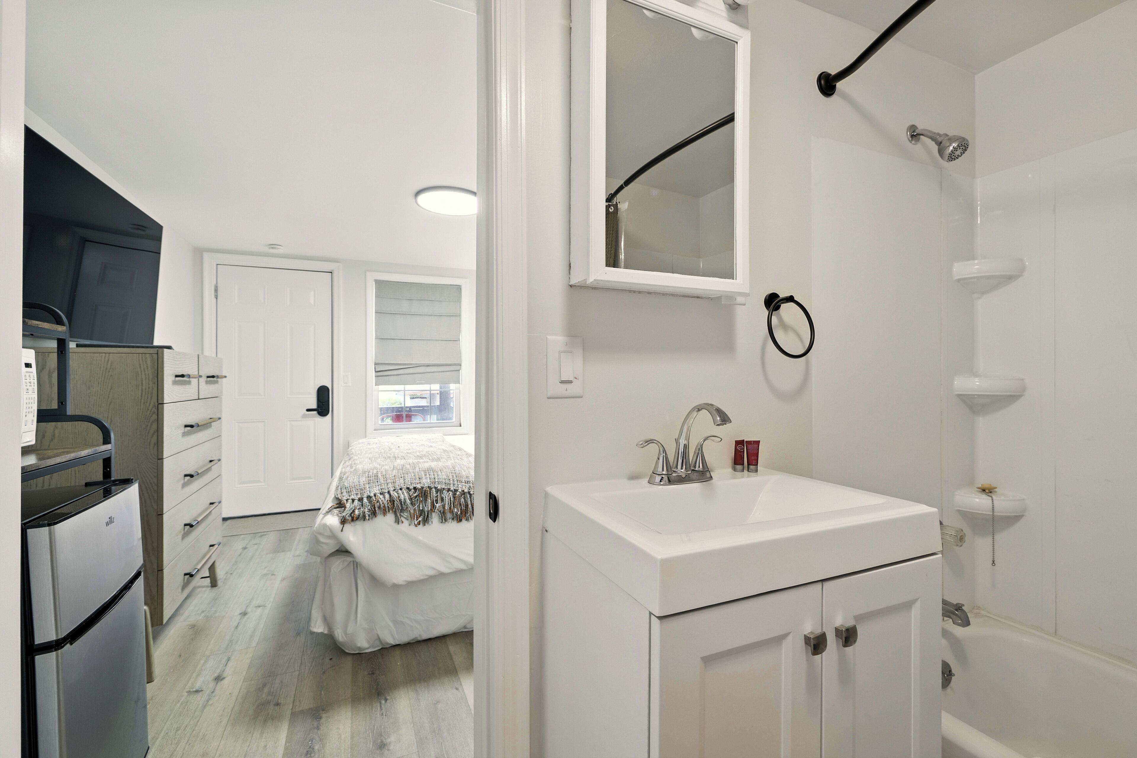 A compact, modern bathroom with a white sink, mirror, and shower.