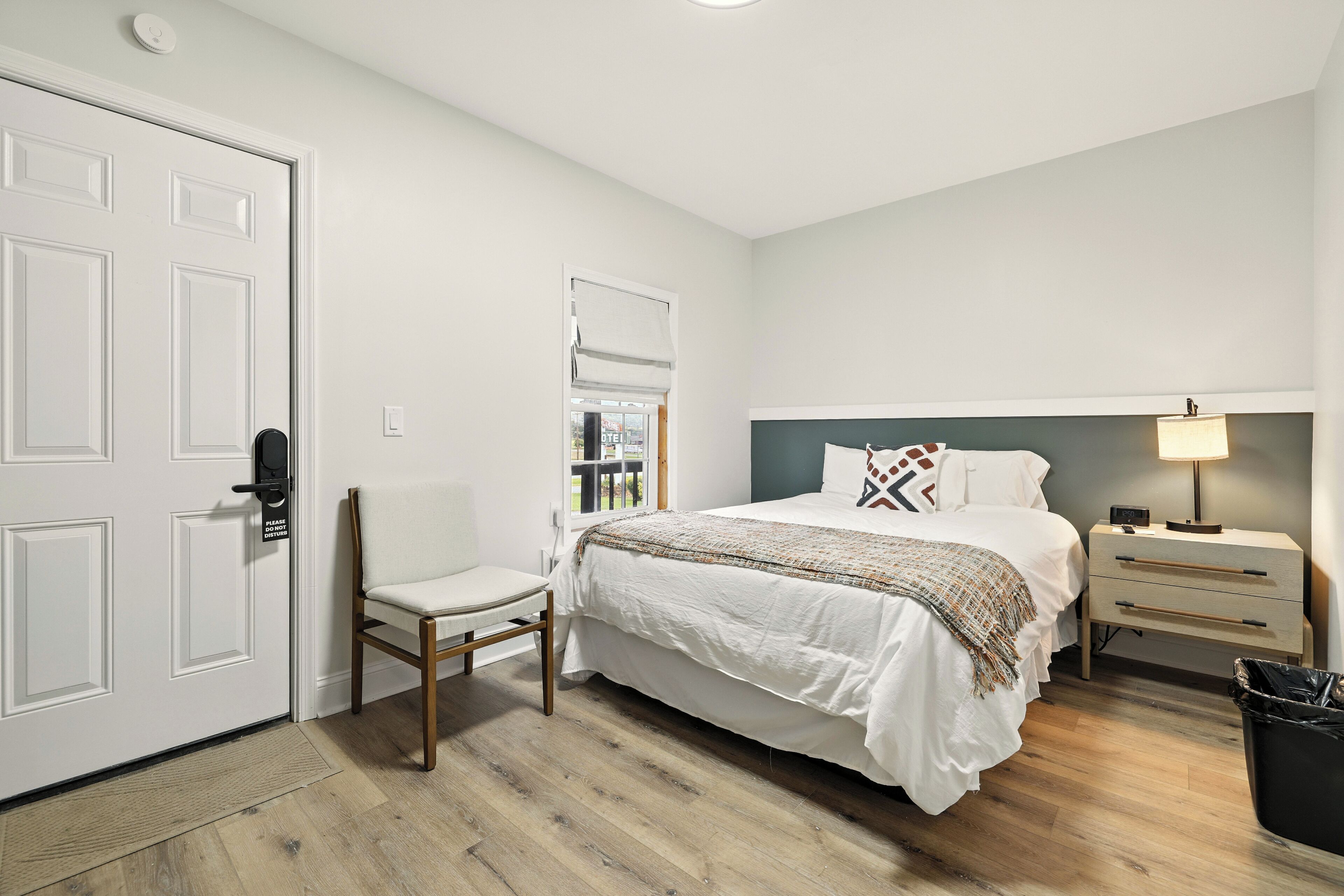A bedroom with a bed, bedside table, chair, and a door.