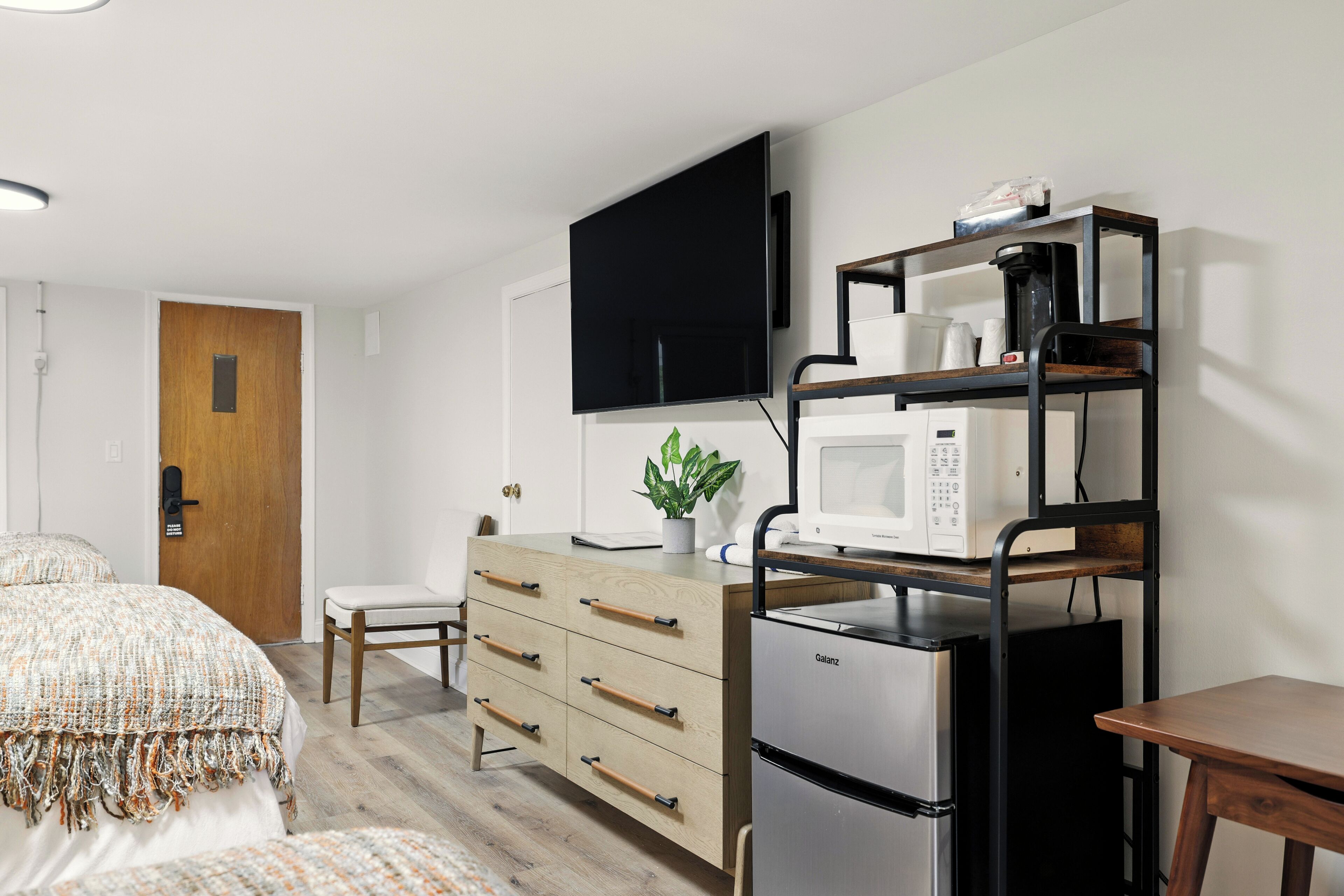 Un dormitorio moderno con cama, cómoda, televisor, microondas y cafetera.