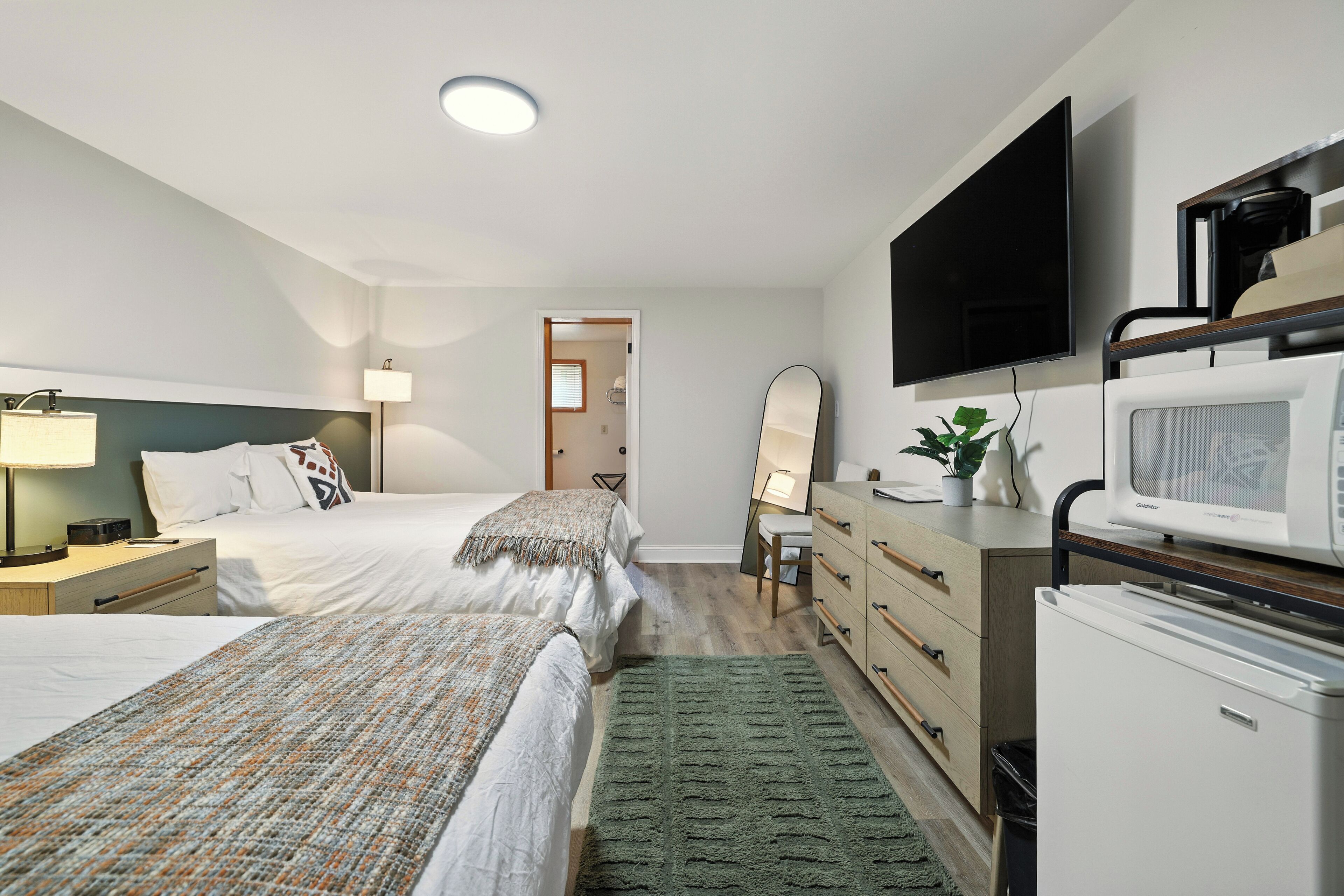 A hotel room with two beds, a desk with a computer, a flat-screen TV, a microwave, and a refrigerator.
