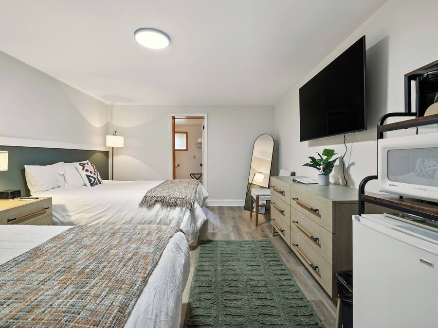 A hotel room with two beds, a desk with a computer, a flat-screen TV, a microwave, and a refrigerator.