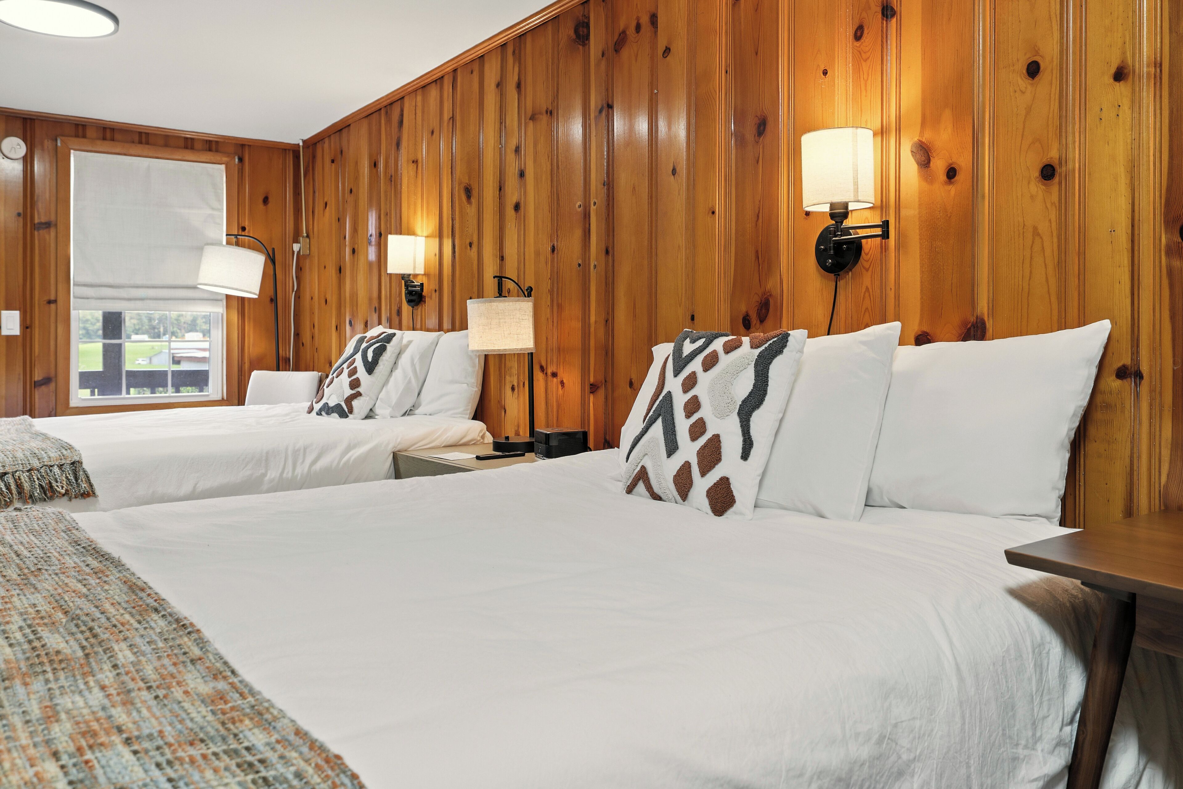 Habitación de hotel con dos camas, paneles de madera y dos lámparas fijadas a la pared.