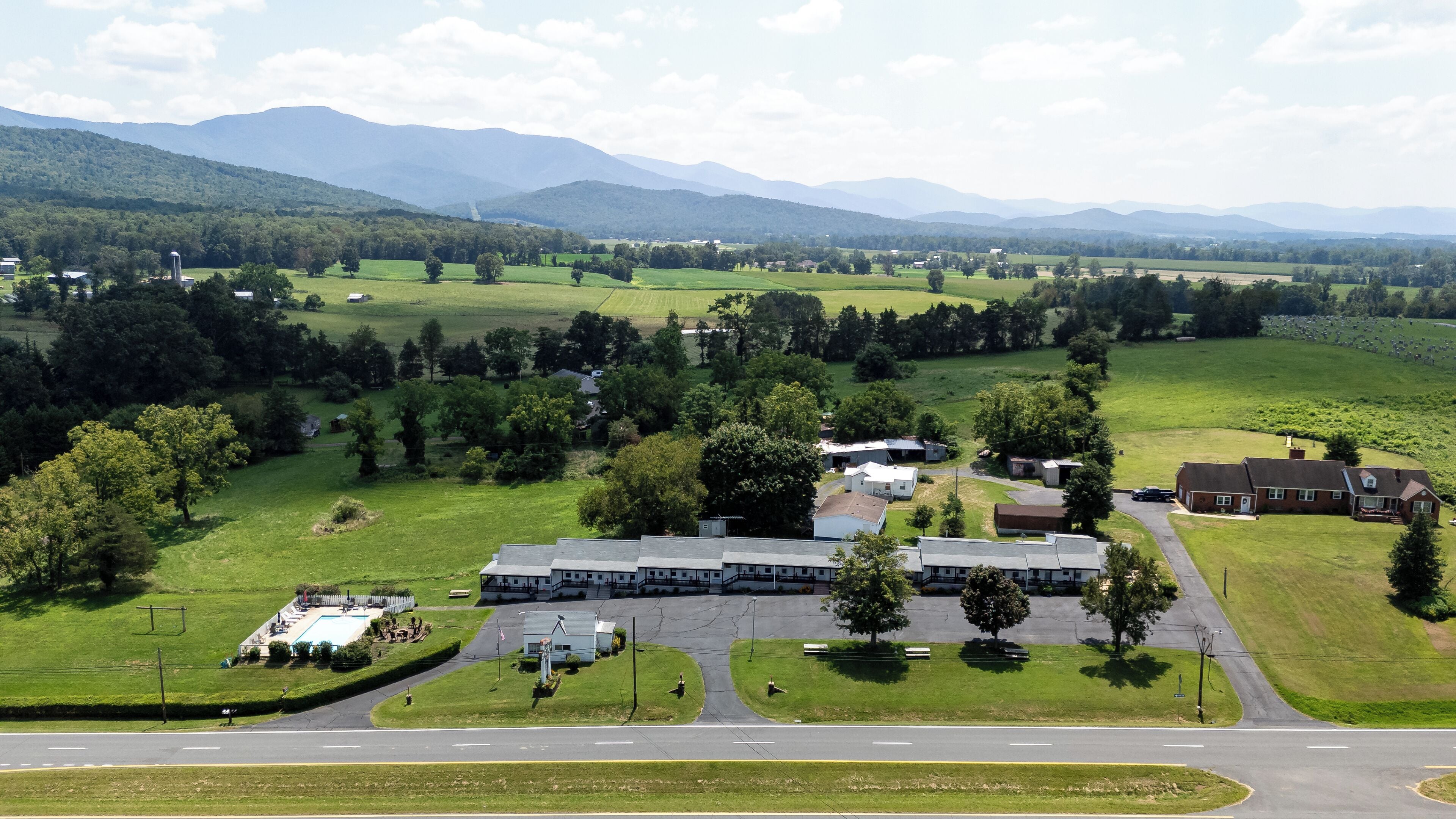 A large building with multiple sections, surrounded by green fields and trees.