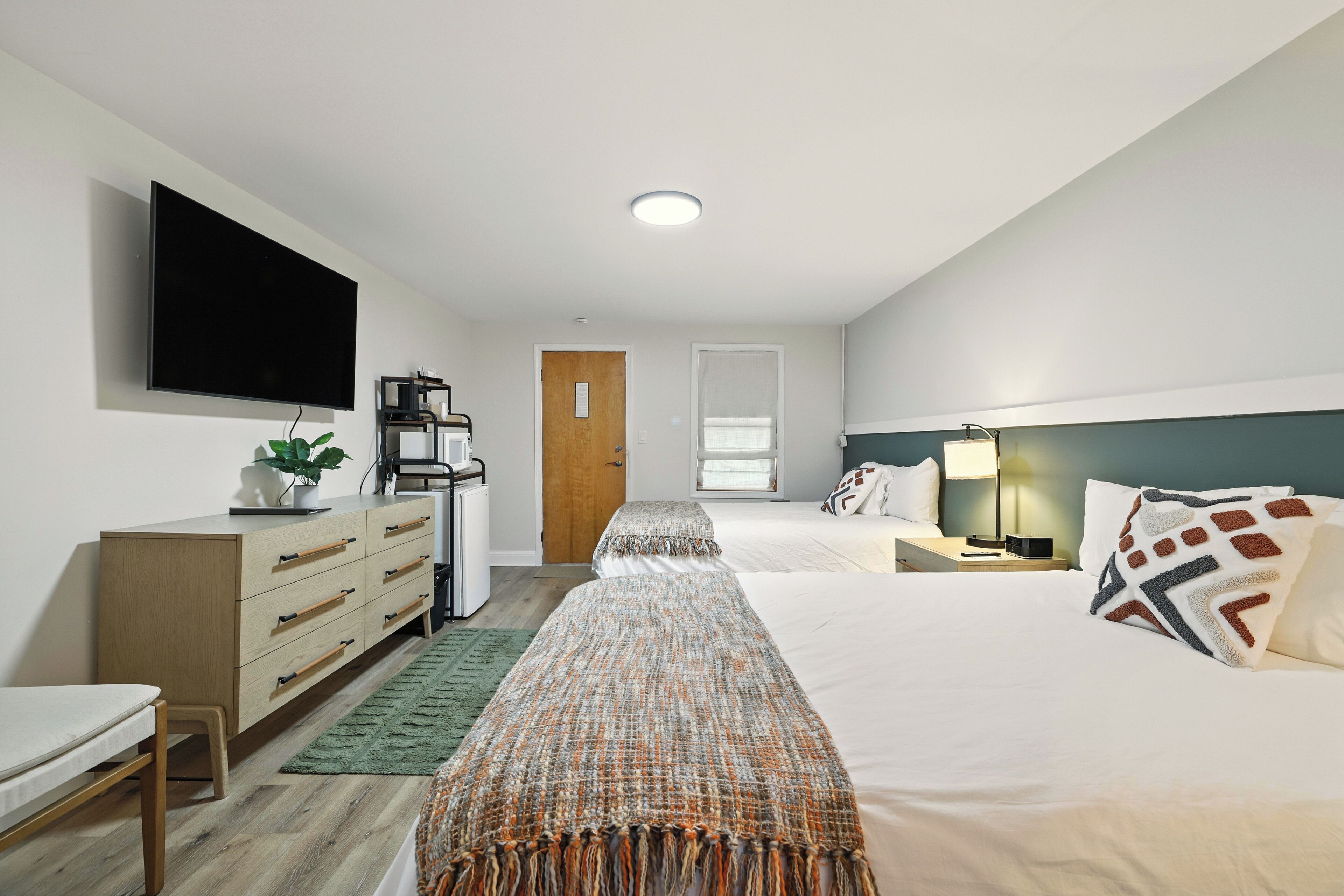A modern hotel room with a bed, bedside table, lamp, and a TV mounted on the wall.