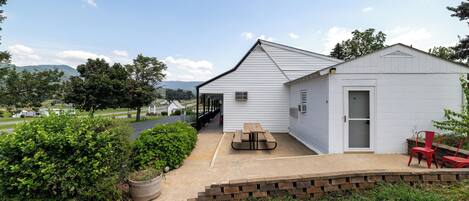 A white building with a covered patio area, a picnic table, and red chairs.
