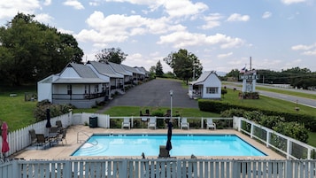 Un motel con piscina, asientos exteriores y una carretera al fondo.
