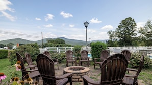 A patio area with Adirondack chairs arranged around a stone fire pit, overlooking a pool and mountains. - Hillside (Luray)