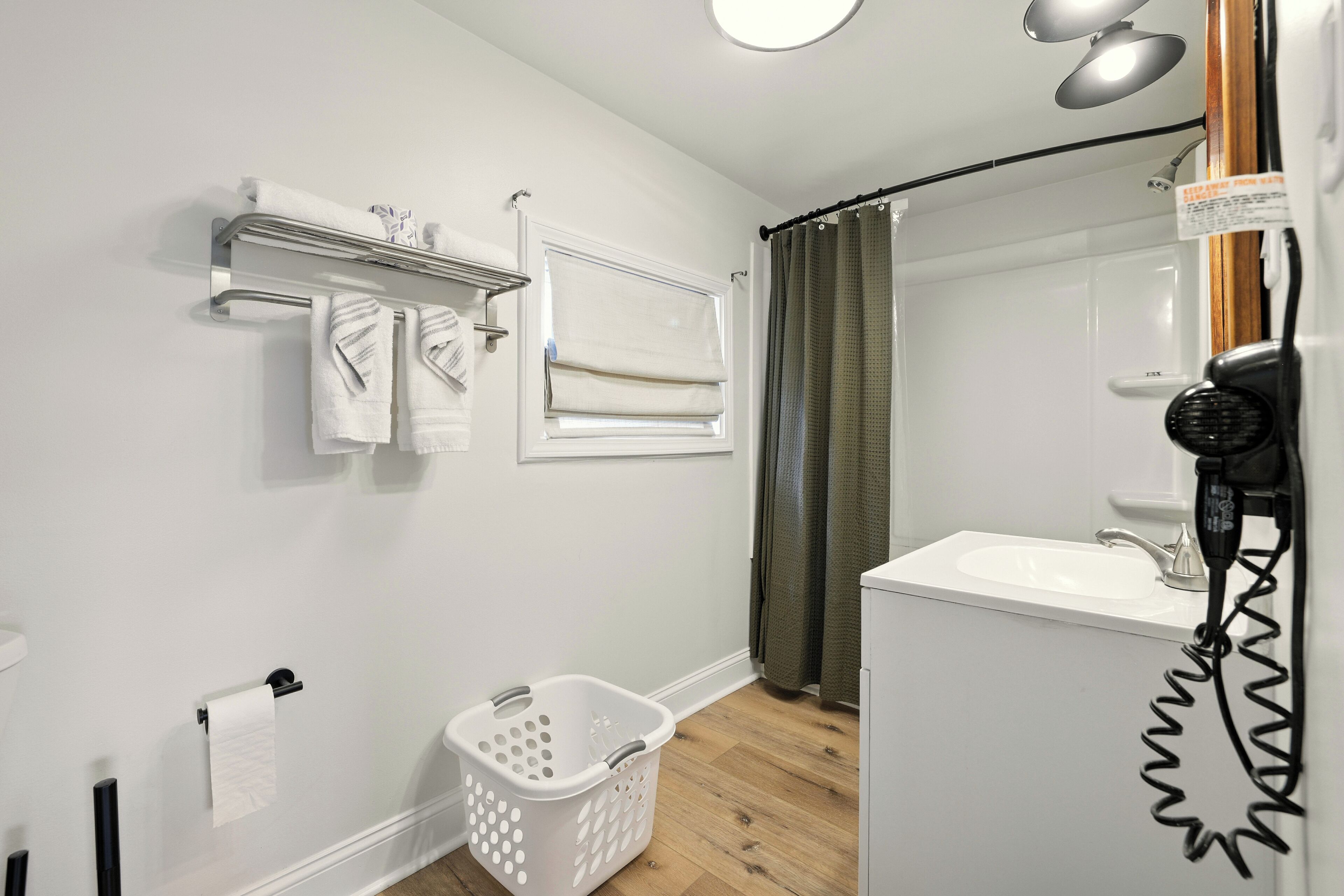 A bathroom with a white sink, a mirror, a towel rack, a shower curtain, and a laundry basket.
