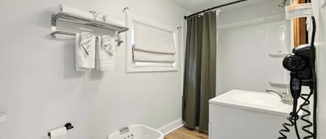 A bathroom with a white sink, a mirror, a towel rack, a shower curtain, and a laundry basket.