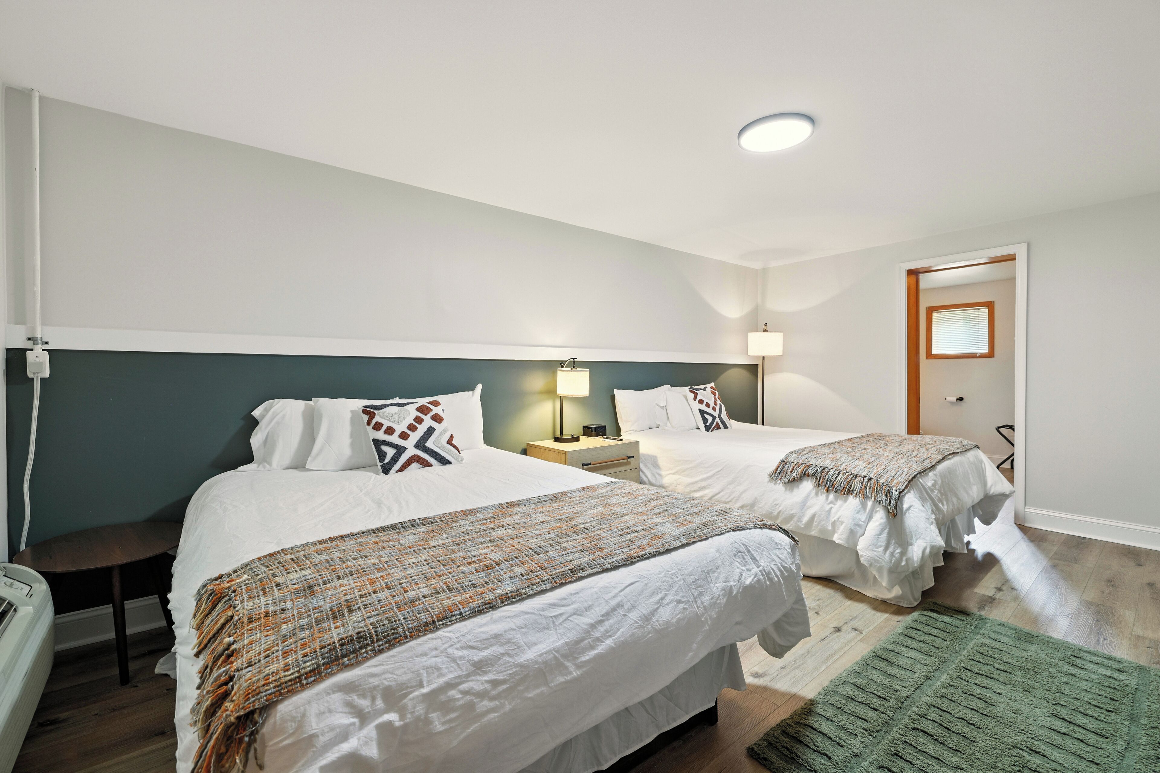 A bedroom with two beds, a green rug, and a nightstand with a lamp.