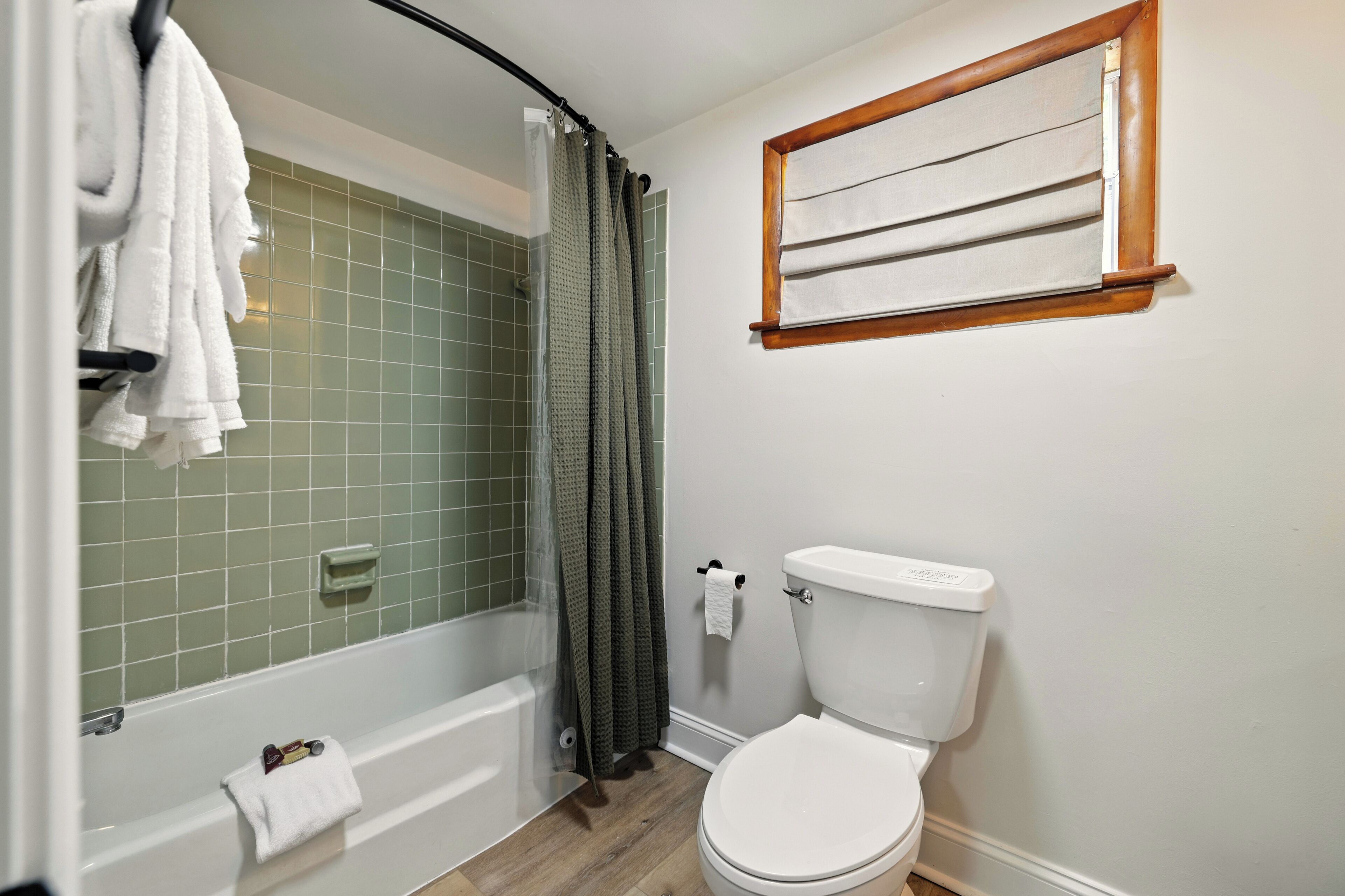 Une salle de bain avec une baignoire, des toilettes et une fenêtre avec un cadre en bois.